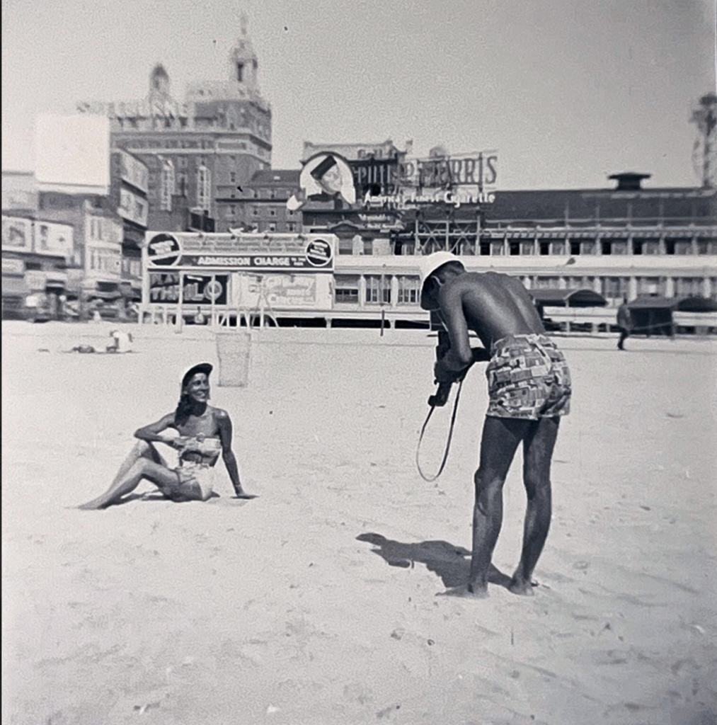 man taking picture of woman lounging on beach shore.